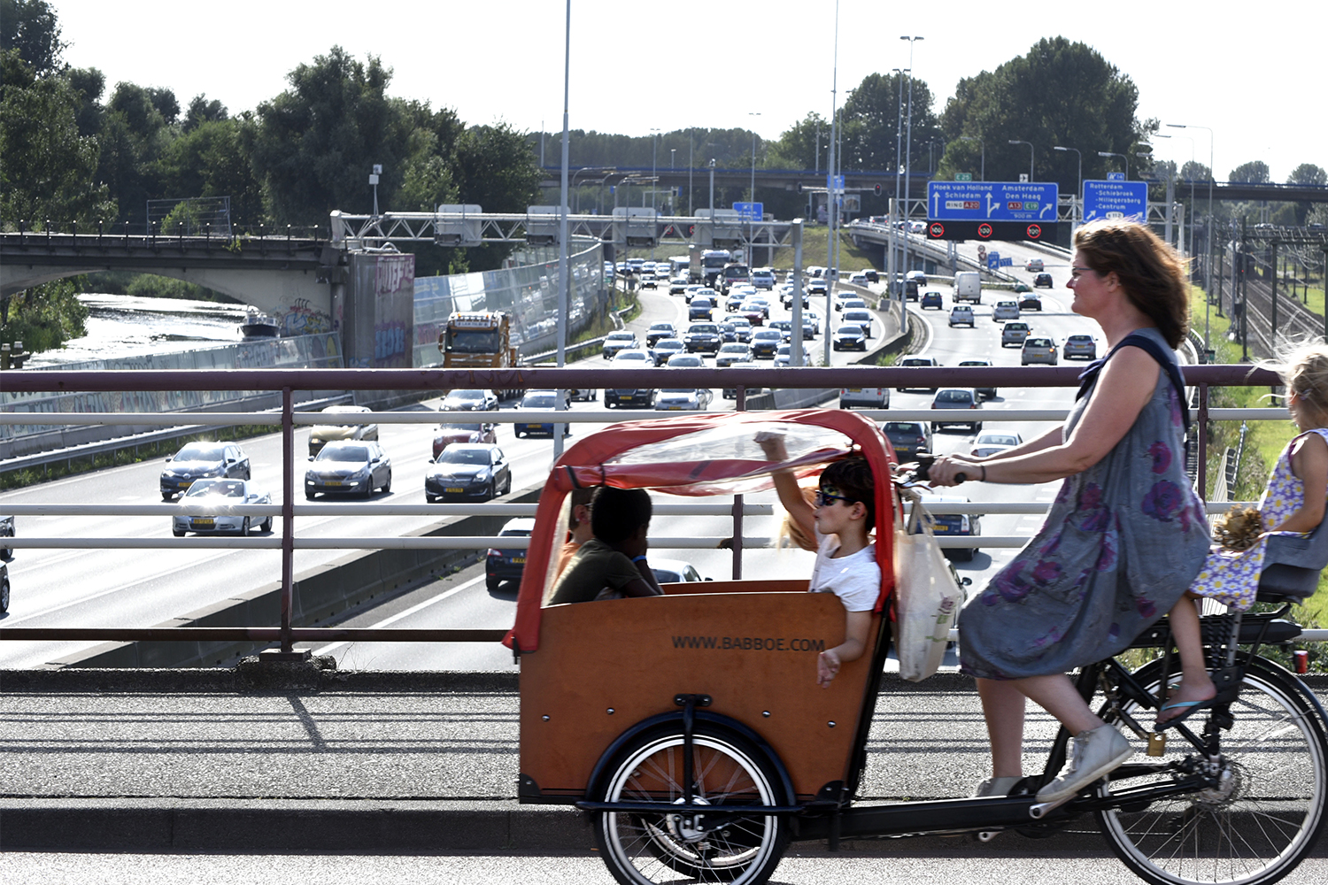 Een vrouw fietst met haar kinderen over een viaduct over een snelweg in Nederland.