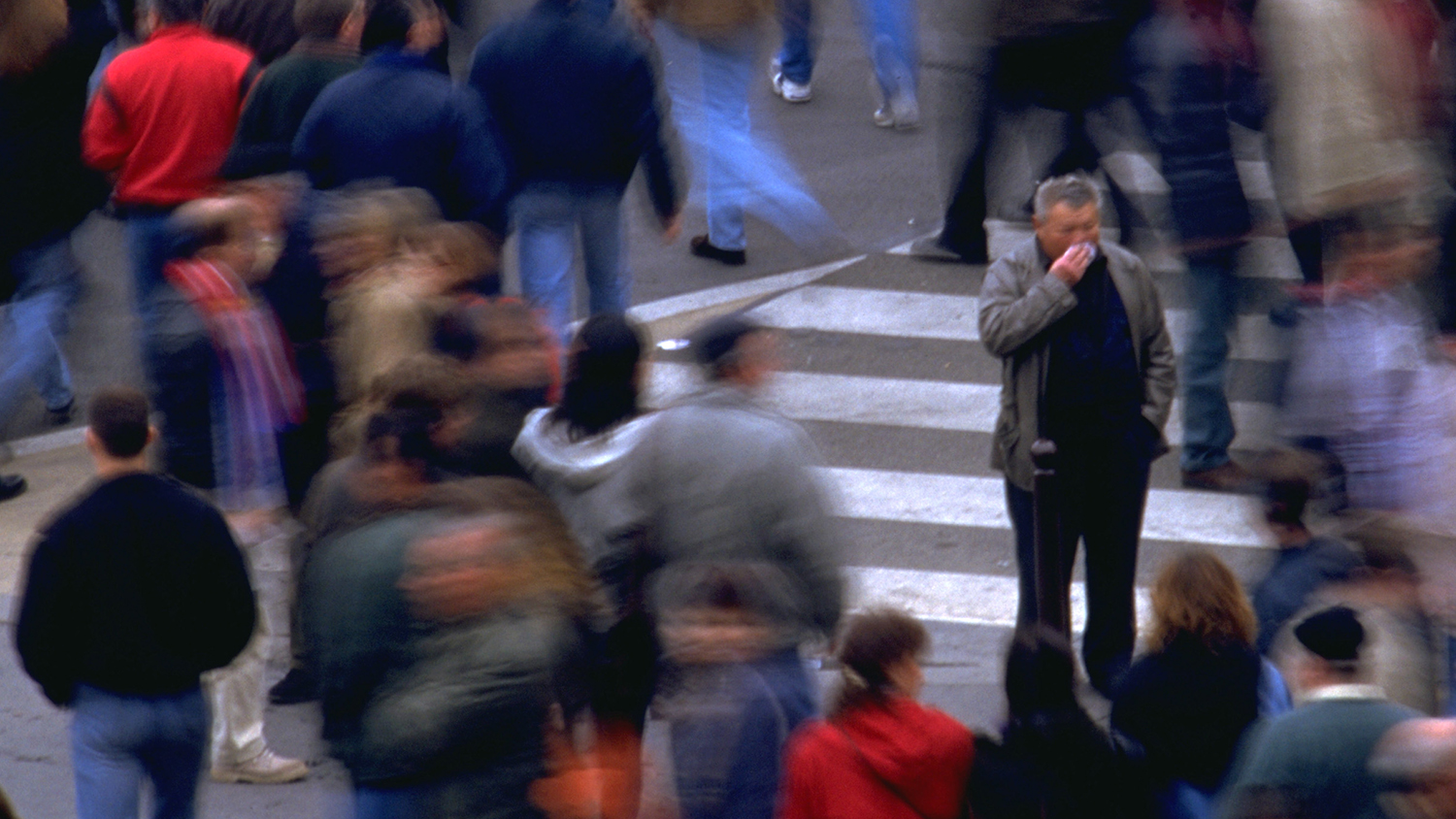 A busy street with a lot of people. A man blows his nose.