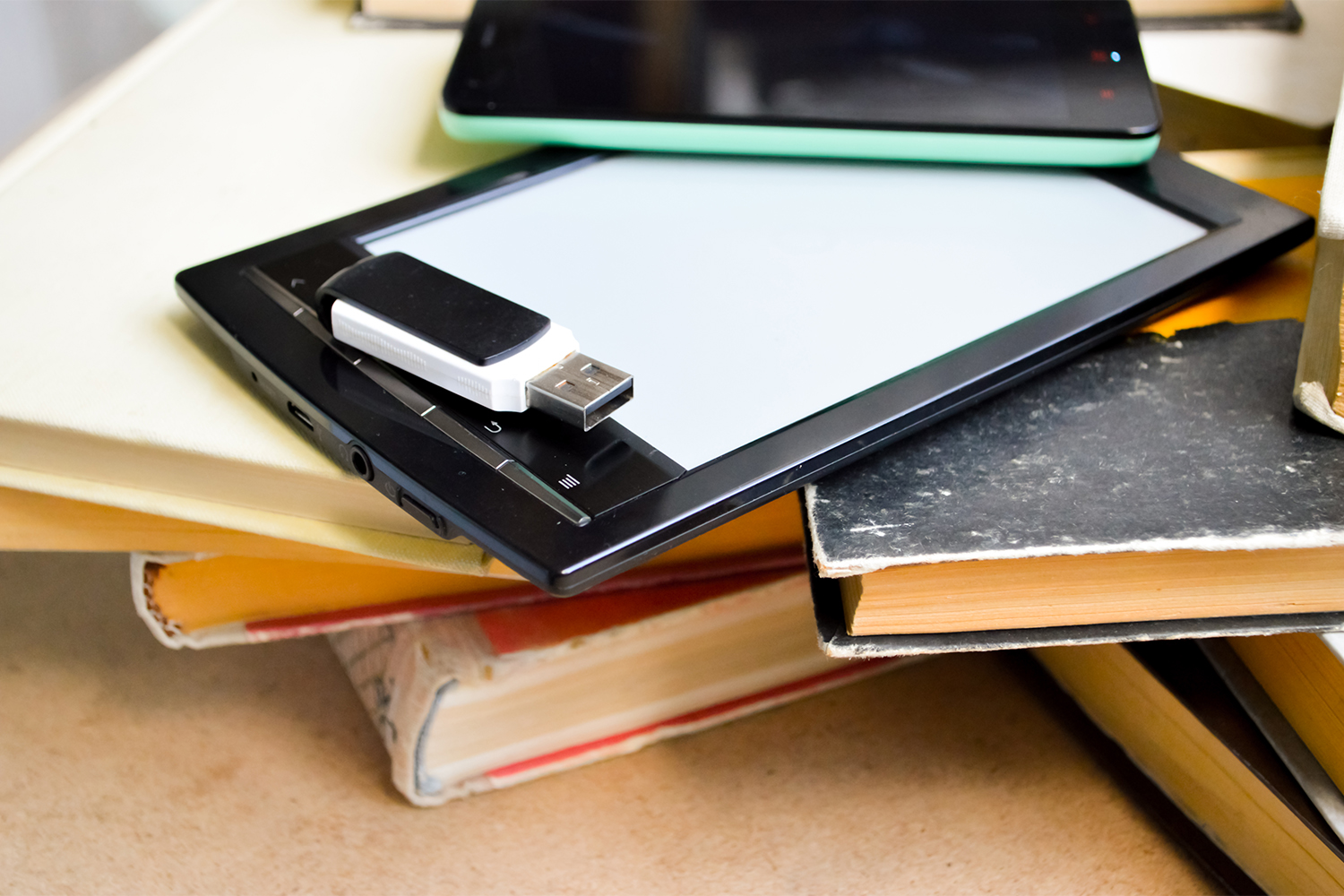 A close up of a stack of books with a tablet, smartphone and a flashdrive on top. 